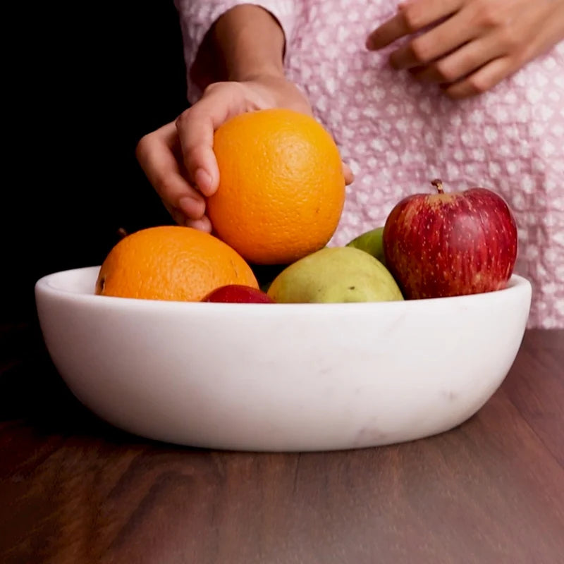 White marble dual-purpose Urli fruit bowl styled on a dining room table