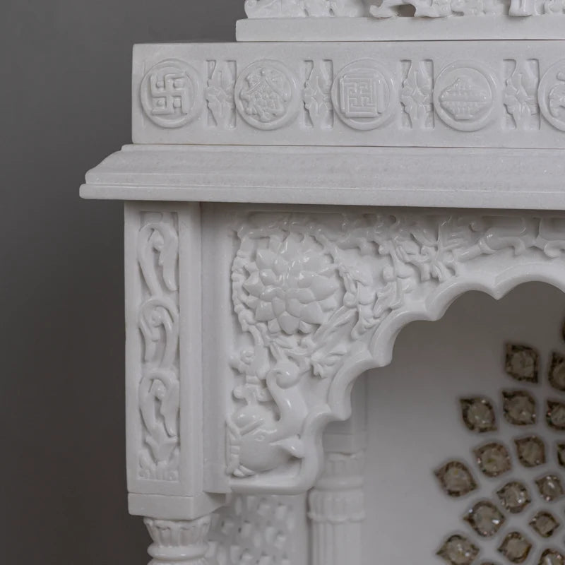 Close-up of golden chakra and carved pillars on marble pooja mandir