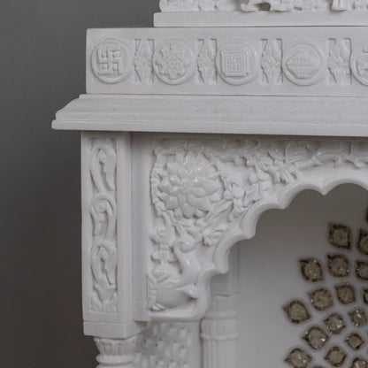 Close-up of golden chakra and carved pillars on marble pooja mandir